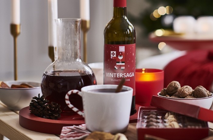 Galds ar Ziemassvētku gardumiem, kūpošu augļu dzērienu baltā krūzē, karafi, pudeli, svecēm.