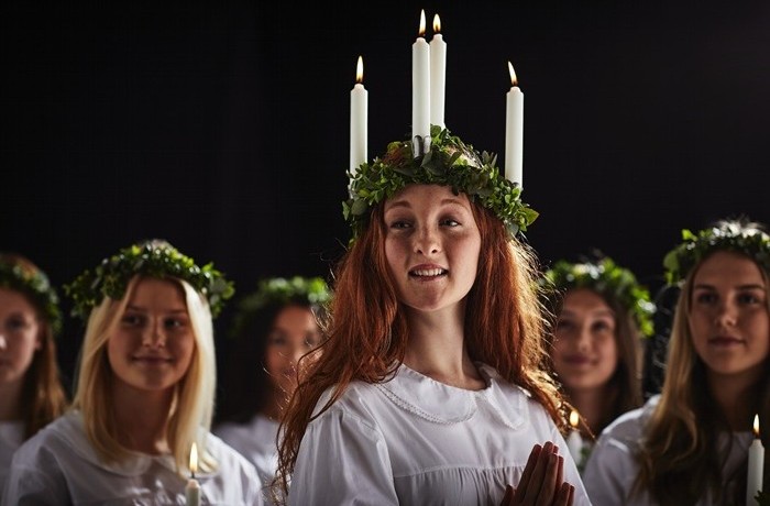 Baltās drānās tērpušās jaunas sievietes ar zaļiem vainagiem galvā, kas piedalās svētās Lūcijas dienas svinībās. Vienai no viņām galvā ir vainags ar svecēm.        