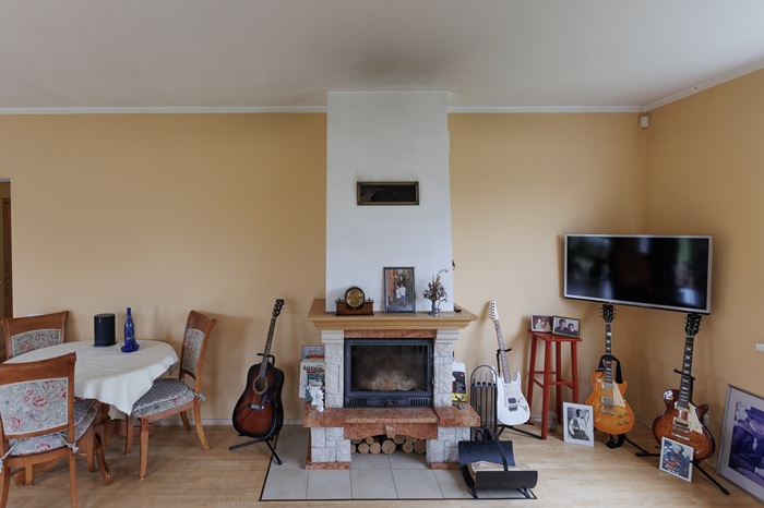 Гостиная до преображения: круглый обеденный стол стоит у камина, рядом четыре гитары и картины в рамках, в углу закреплён телевизор.