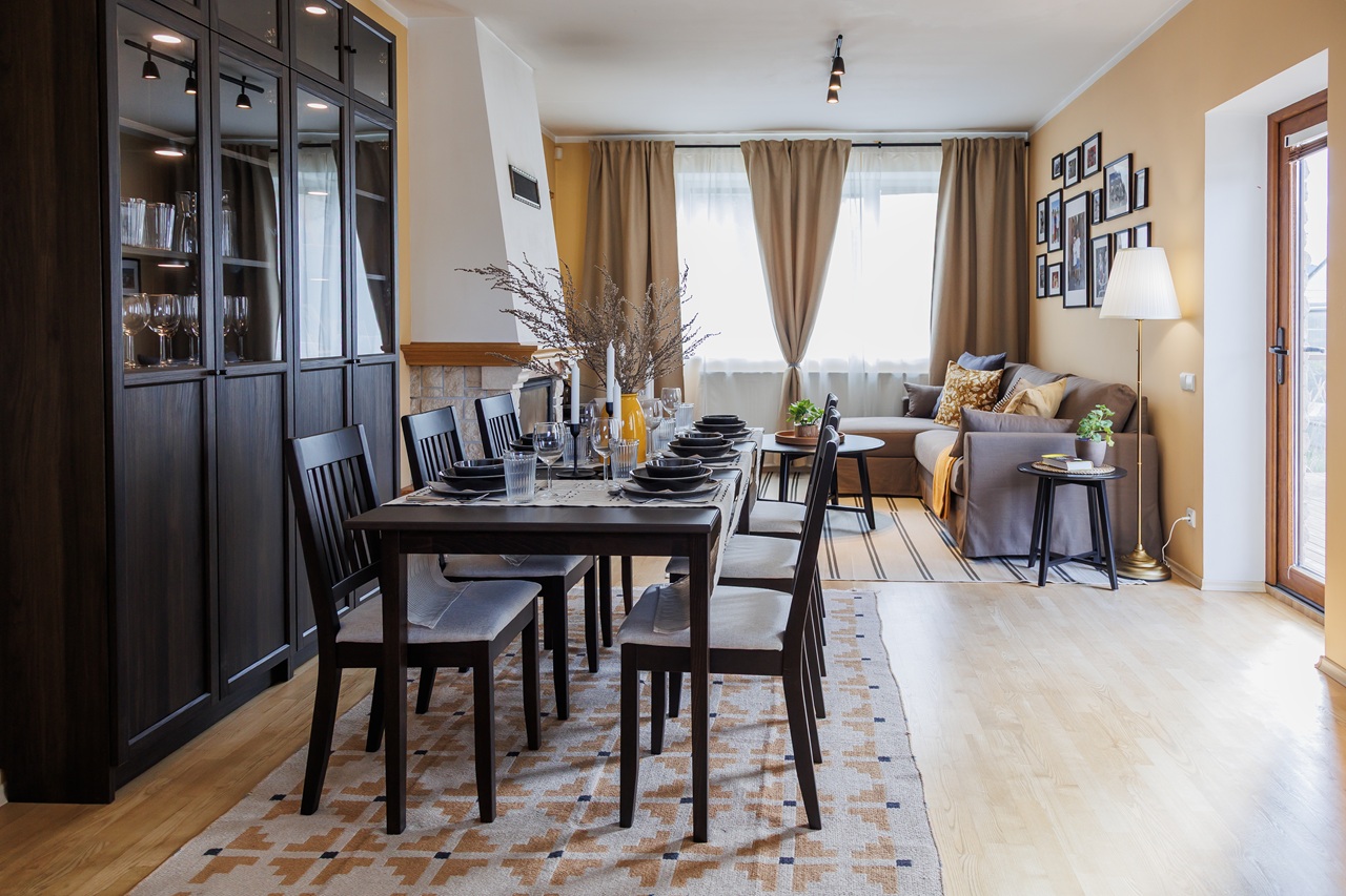 Гостиная и обеденная зона после ремонта: длинный тёмно-коричневый стол с шестью стульями, тёмно-коричневый шкаф-витрина со стеклянными дверцами, угловой диван и журнальный столик.