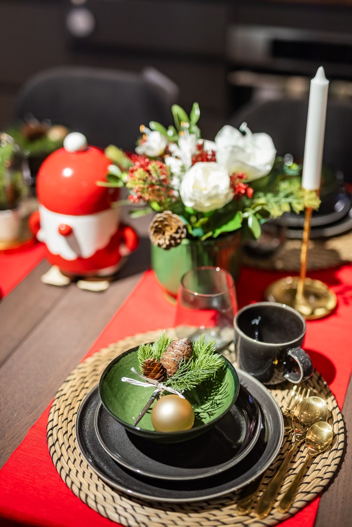 Close-up of a Christmas table setting with black plates, green napkins, red accents and a festive floral arrangement.