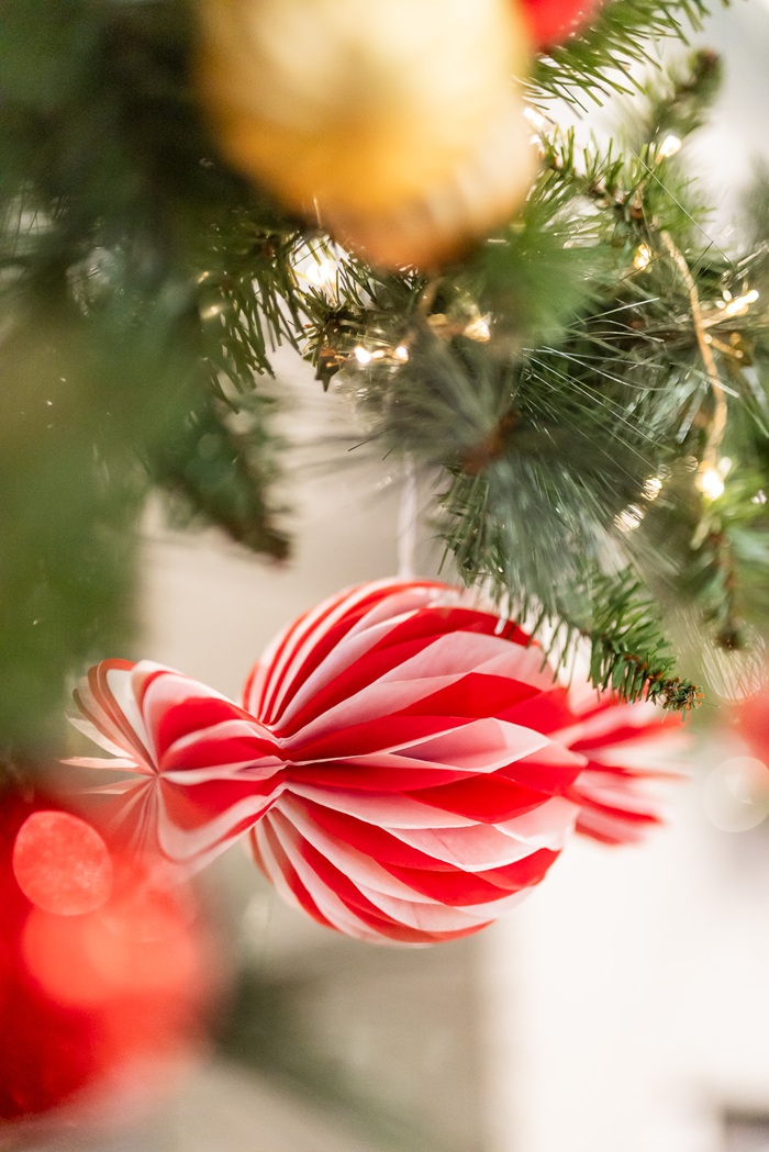 Close-up of a red striped Christmas ornament hanging from a holiday garland with soft lights in the background.