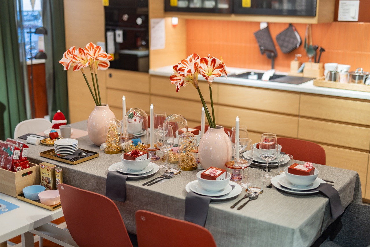 A festive dining table in a modern kitchen, decorated with pink vases of amaryllis, glass domes filled with ornaments, candles and neatly arranged table settings.