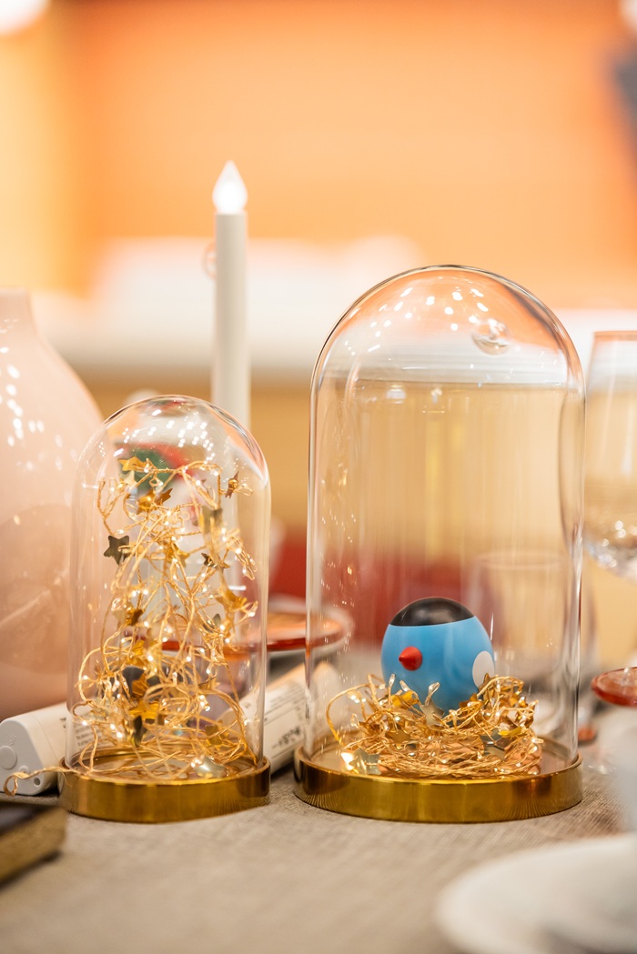 Close-up of decorative glass domes filled with small ornaments and gold accents, with white candles placed beside them.
