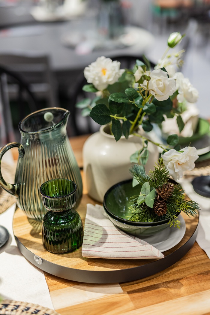 Close-up of a green glass jug, white flower arrangement and layered green plates on a festive table.