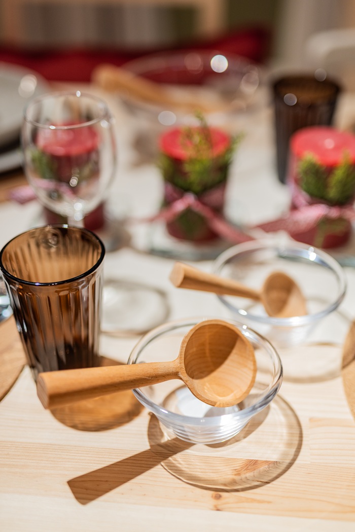 Close-up of amber-toned glassware, festive greenery and small red decorations arranged on a holiday dining table.