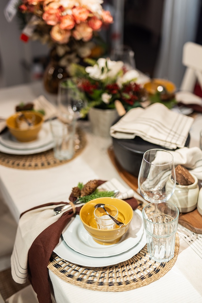 A decorated Christmas table with layered plates, warm floral arrangements, greenery and candles set in a cosy dining area.