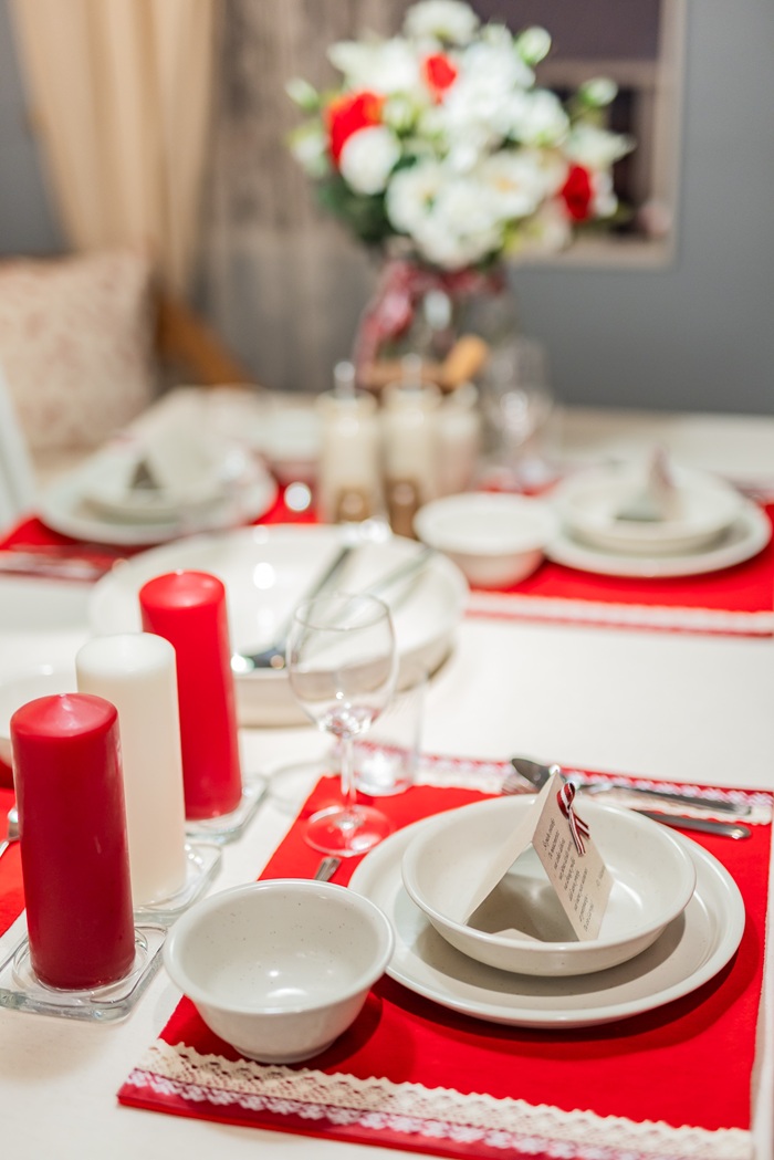 A decorated holiday table with red candles, white plates and a floral centerpiece in red and white tones.