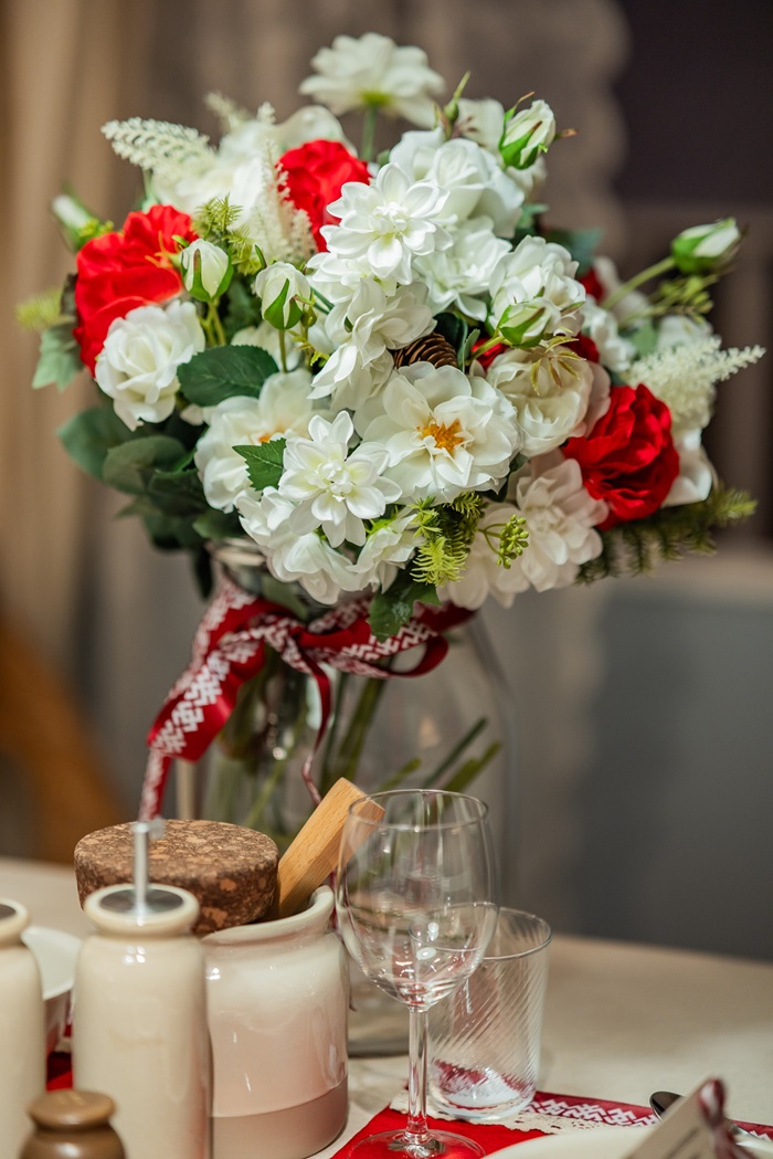 Close-up of a red and white floral centerpiece in a glass vase on a festive dining table.