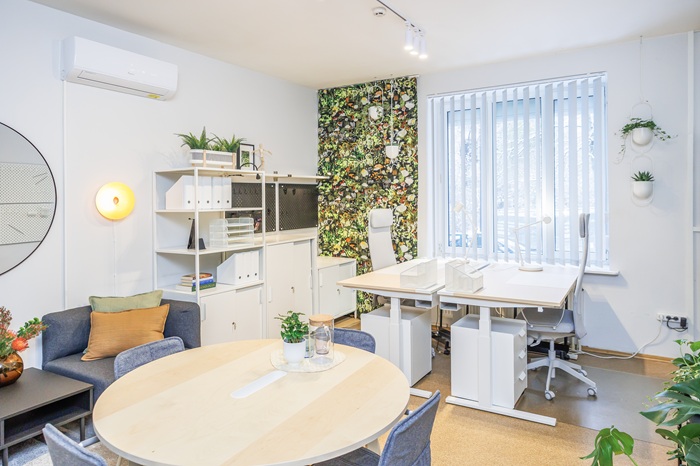 Aiškiai atskirtos zonos priimamajame: apvalus stalas susitikimams su svečiais patalpos centre ir darbuotojų stalai prie lango.