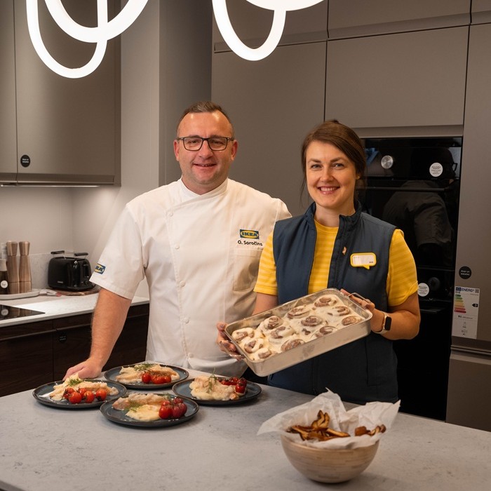 Два эксперта ИКЕА за столом в магазине с тёмно-серой посудой GLADELIG на плетённой подставке.