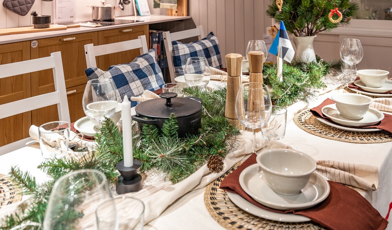 Valge laudlinaga jõululaud, mis on kaunistatud käbisid täis roheliste roheliste kuuseoksavanikutega. Laual on valged taldrikud ja kausid helepruunide lauamattide ja punakaspruunide salvrätikute peal.