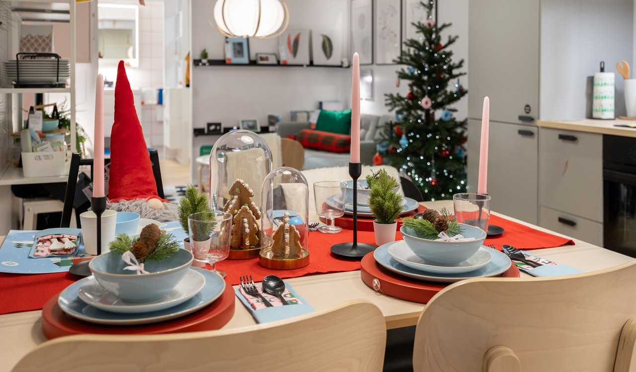 Jõululaud, millel on helesinised kausid, punased lauamatid ja roosad küünlad minimalistlikes mustades küünlajalgades. Taustaks on värviliste kaunistustega jõulupuu ja helehallid köögikapid.        