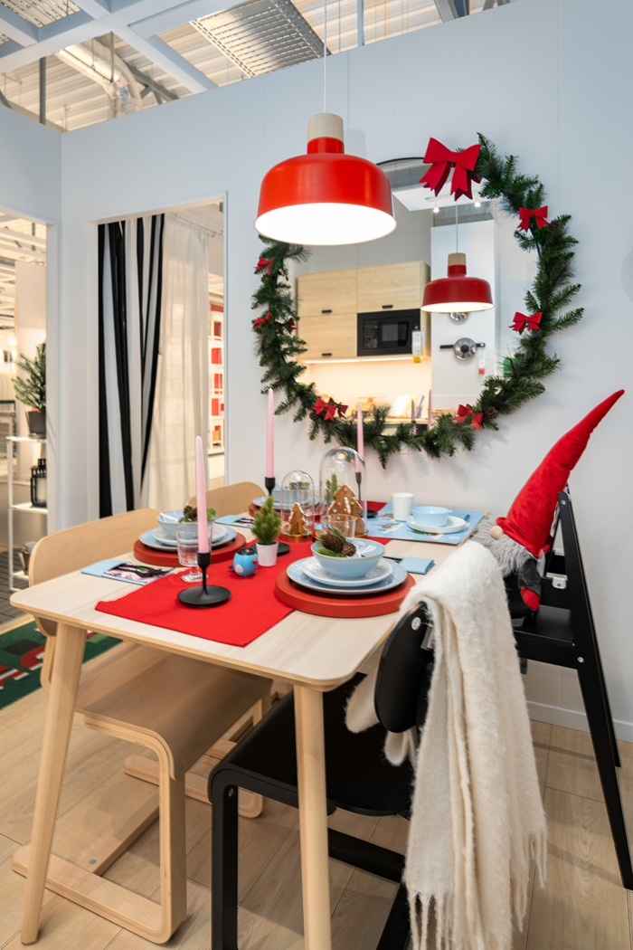 Heledast puust laud, millel on punane linik ja lauamatid. Toa seinal on peegli ümber pärg. Laua kohal rippuv punane lamp peegeldub peeglis.        