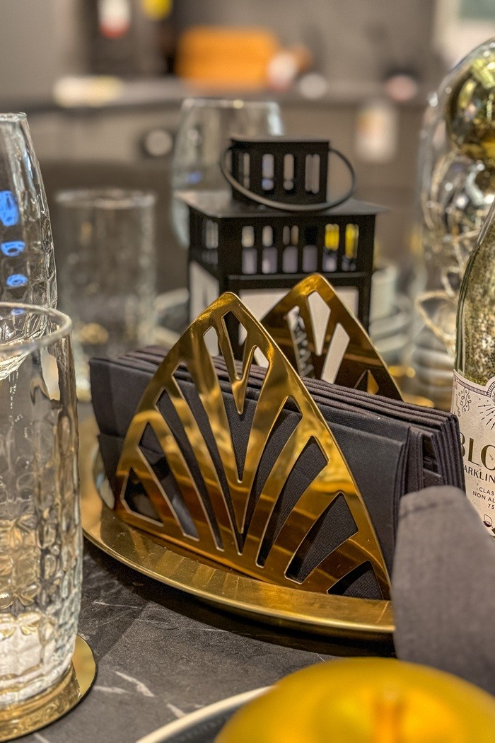 Kuldne salvrätikuhoidja, milles on tumehallid salvrätikud. Kirjad klaasid ja kuldsed kaunistused rõhutavad kaetud laua pidulikkust.