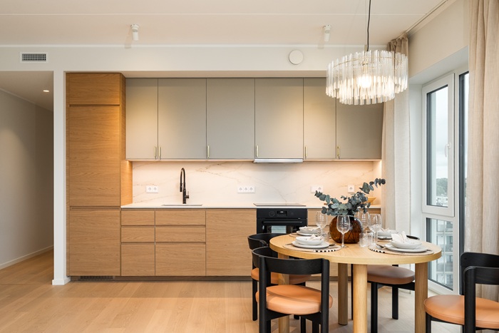 A Scandinavian style kitchen with light wood cabinets, beige upper cupboards, and black chairs around a small round table.