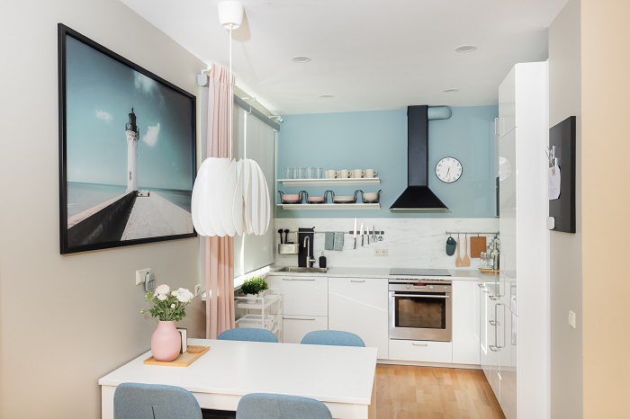 Gaiša, moderna virtuve ar ēdamgaldu, gaišām mēbelēm un maigiem pasteļtoņu akcentiem.