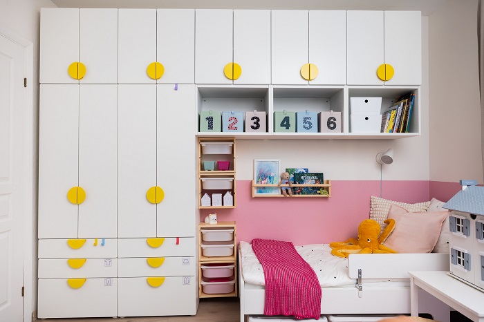 Bērnistaba ar rozā sienām, plauktiem rotaļlietām, rakstāmgaldu un rotaļīgām interjera detaļām.