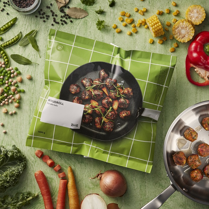 Iepakojums ar IKEA dārzeņu bumbiņām uz gaiši zaļa fona, apkārt atrodas dārzeņi, kas ir to sastāvā.   