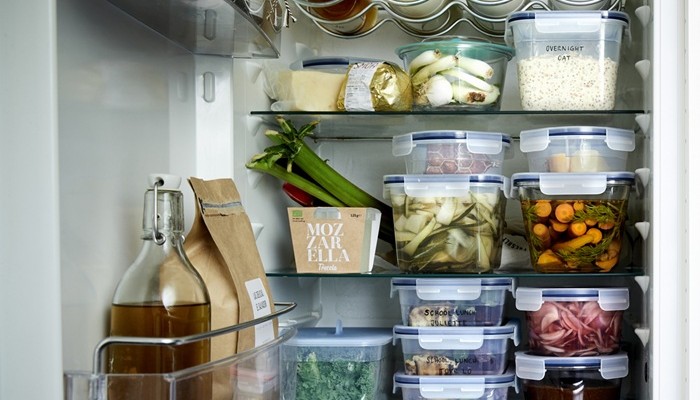 Lähivõte täiuslikult korrastatud külmkapist, kust paistavad läbipaistvad säilituskarbid ja korralikult paigutatud klaaspudelid. 