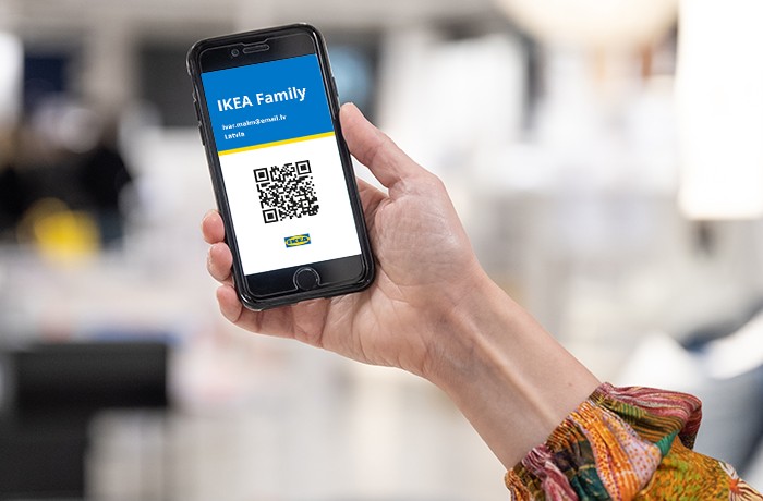 Смартфон в руке. На экране отображается цифровая карта члена IKEA Family с QR-кодом, логотипом IKEA и адресом электронной почты участника.