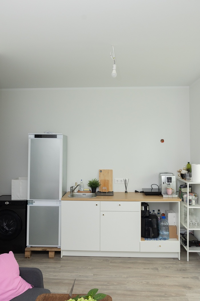 Atvērta tipa virtuve ar virtuves iekārtu, ēdamgaldu un krēsliem gaišā telpā.