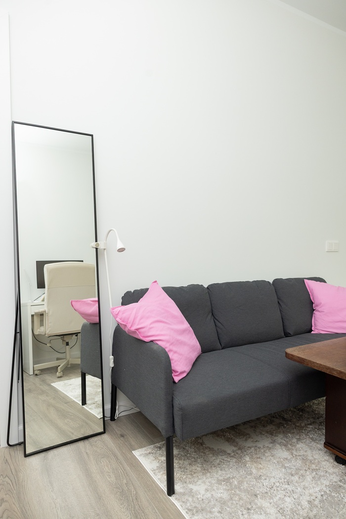 Vienkāršs atpūtas stūrītis ar dīvānu, spilveniem un lielu spoguli pie sienas.