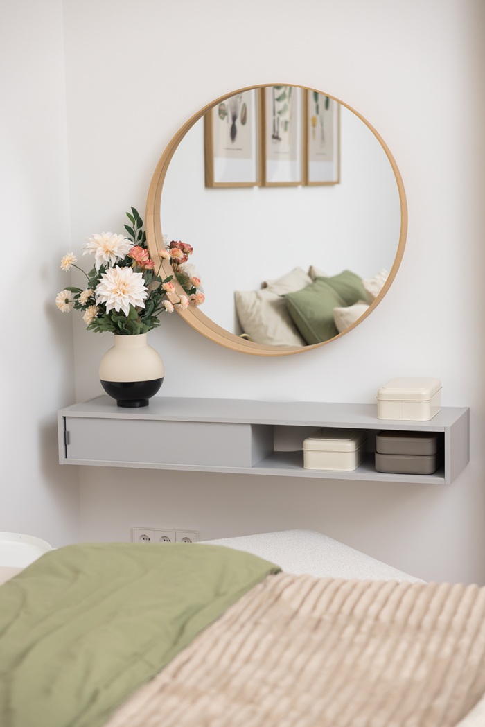 Apaļš spogulis virs sienas galdiņa ar dekoratīviem priekšmetiem guļamistabā.