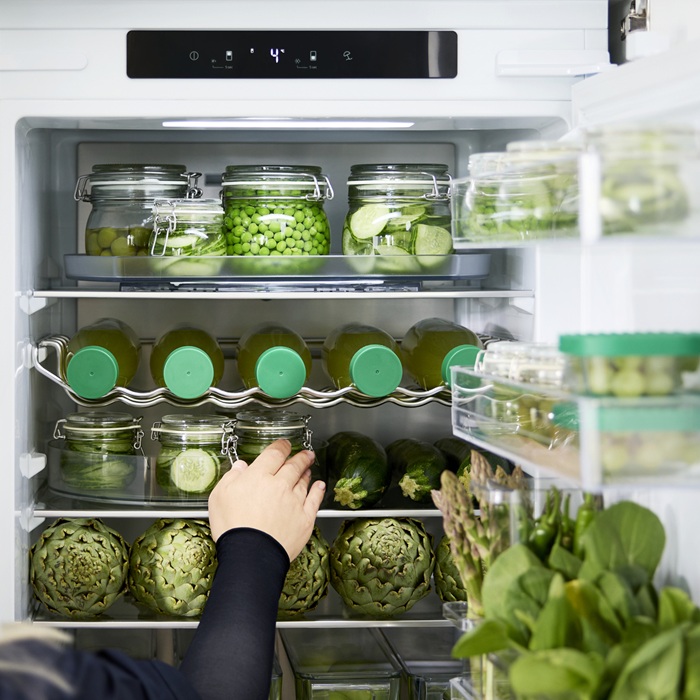Cilvēks sakārto svaigus produktus ledusskapī, izmantojot KLIPPKAKTUS caurspīdīgās uzglabāšanas kastes.
