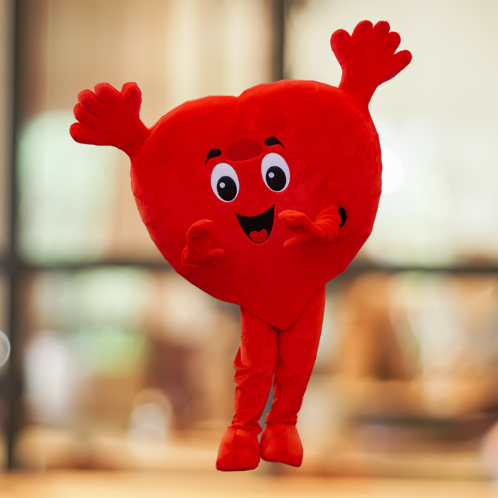 Весёлый персонаж-талисман FAMNIG HJÄRTA в форме сердца на размытом фоне.