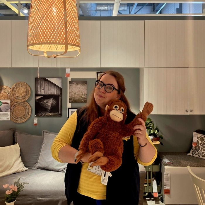 Naine IKEA näidistetoas hoiab pruuni plüüšist orangutani mänguasja rippuva lambi all.