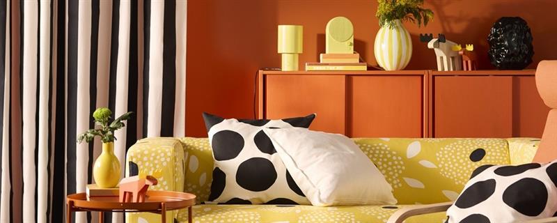 A yellow and white floral-patterned KLIPPAN cover for 2-seat sofa on a sofa in a vivid living room with an orange back wall.