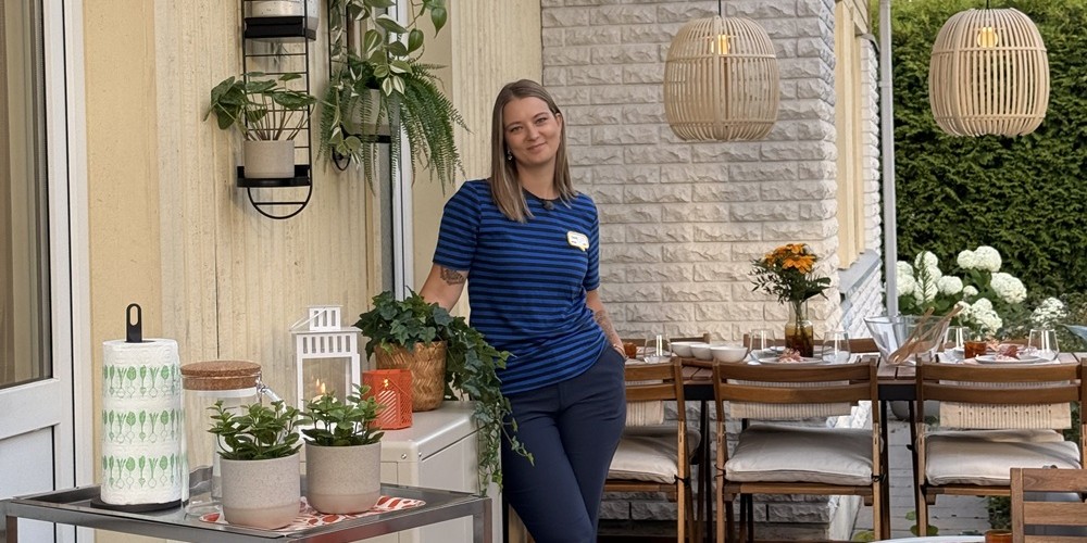 Aiaterrass, kus on valge NÄMMARÖ mooduldiivan ja suur söögilaud toolidega. Kogu sisustus on heledates ja beežides toonides, millele lisavad särtsu oranžid padjad ja rohelised taimed, mis ripuvad seinal.
