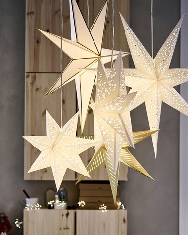 A group of glowing STRÅLA star-shaped pendant lamps in white and gold hangs together, creating a warm and festive atmosphere in a room.