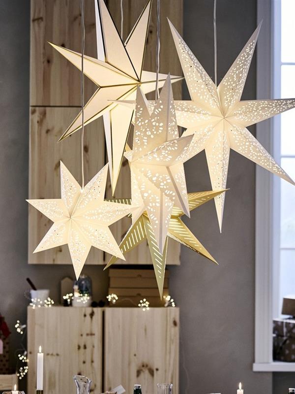 A group of glowing STRÅLA star-shaped pendant lamps in white and gold hangs together, creating a warm and festive atmosphere in a room.