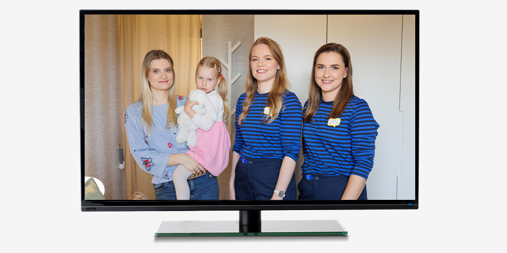 Television screen showing a mother with their daughter and two IKEA interior designers standing together in a bedroom, smiling at the camera.