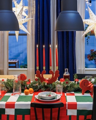 A cosy Christmas table with red-and-green patterns, star-shaped pendant lamps and a simple Scandinavian candelabra.