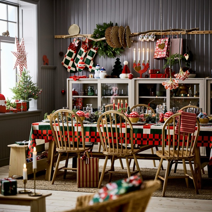 A long table with six wooden chairs stands in a traditionally styled dining room. The space is decorated in green, red and white, and the table is laid with a festively checked Christmas tablecloth.