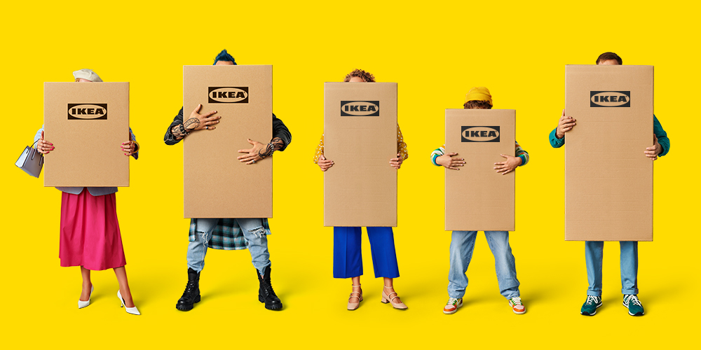 Three people stand against a yellow background, each holding flatpacks with IKEA logos in their hands.